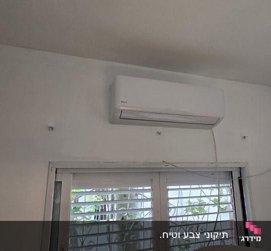 מזגן מותקן על קיר מעל חלון עם תריסים